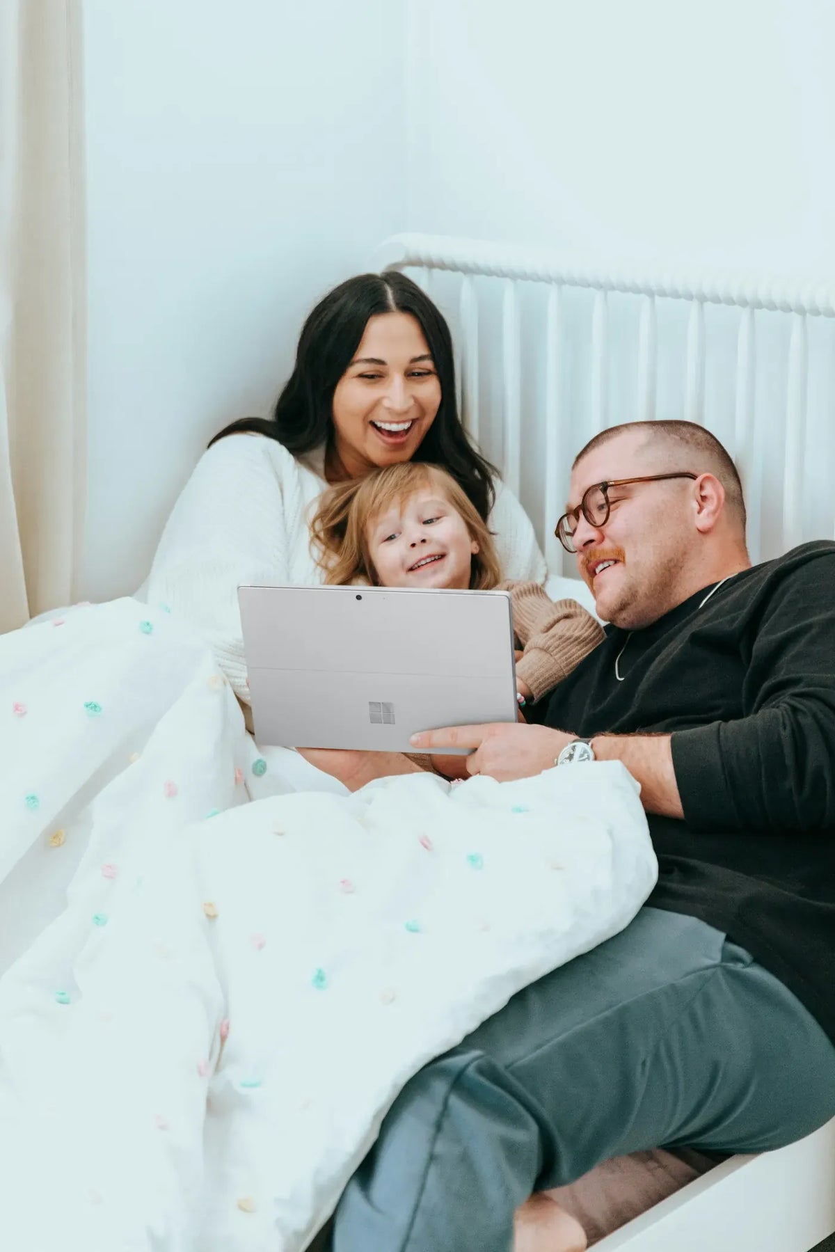Mom, dad and daughter in bed with a tablet