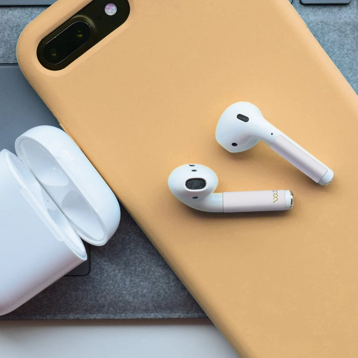 Airpod earbuds, classic, WaveBlock Stickers to reduce EMFs, iPhone with case, Airpod case to the left. Earbuds laying on top of phone.