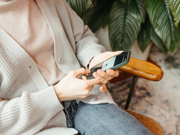 woman sitting in chair while holding cell phone in both hands close to her legs and stomachh