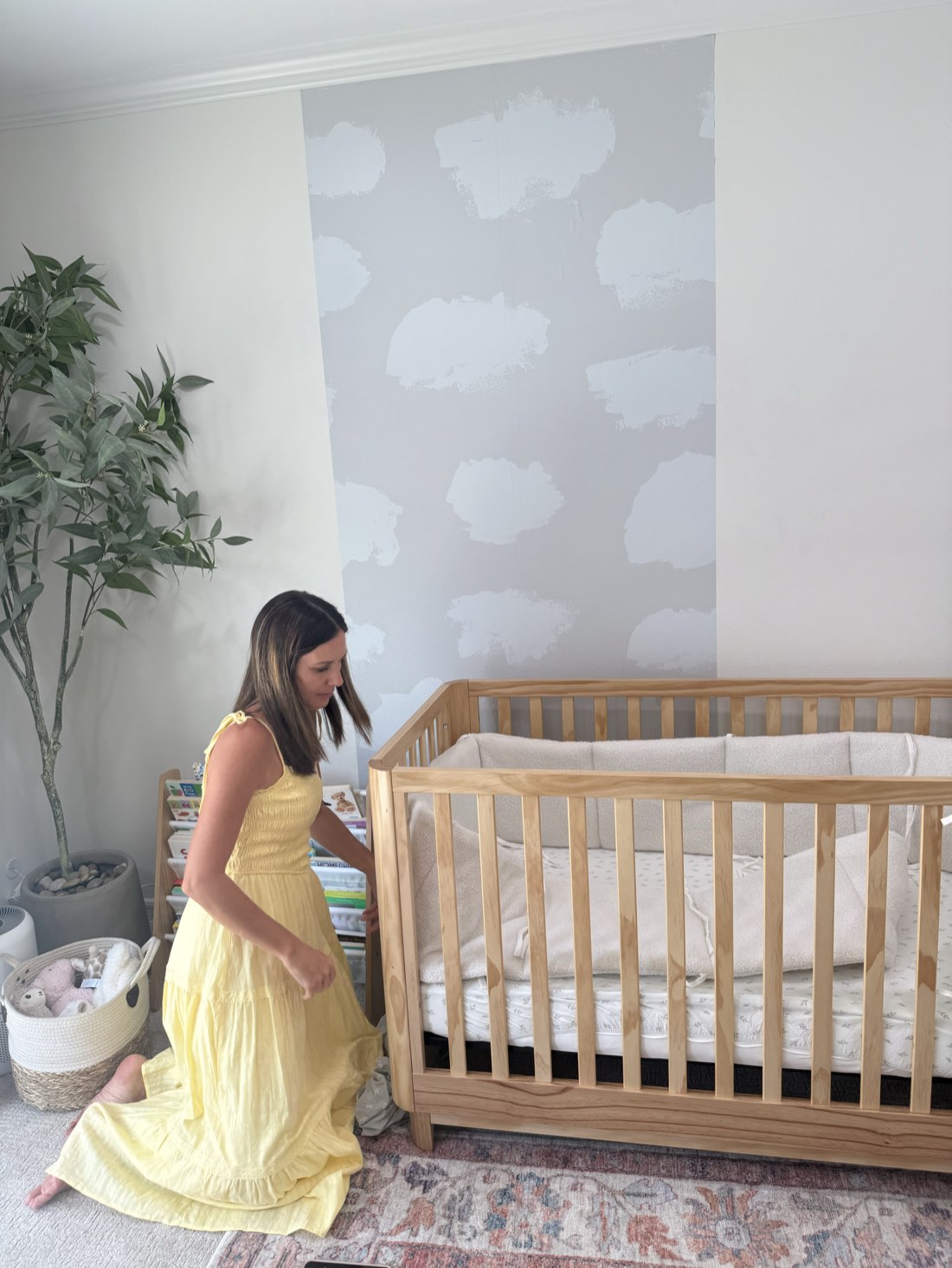 A mother kneeling by the crib in front of a SafeWall Clouds wall